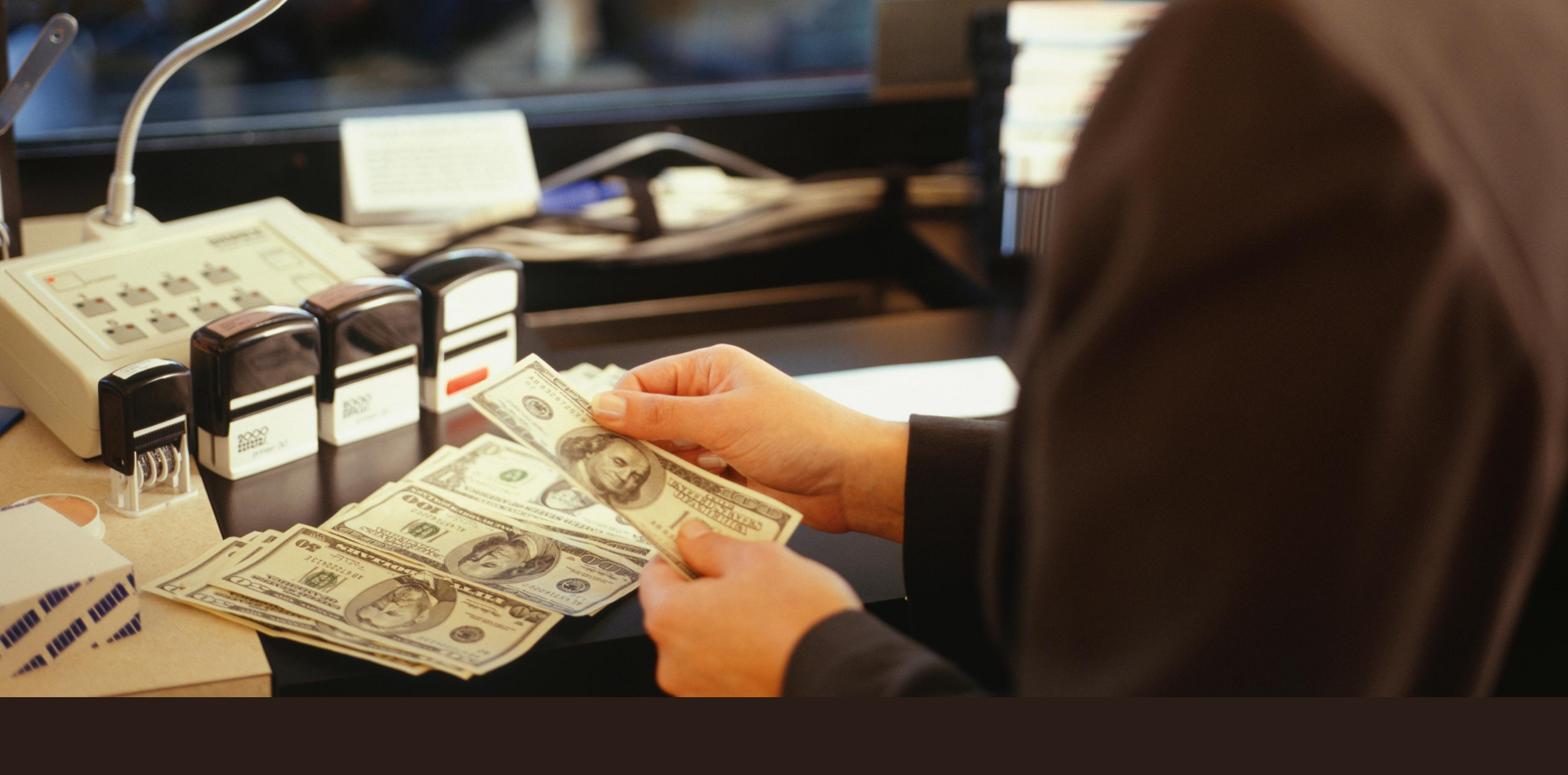 Woman holding 100 dollar bill with bills laid below